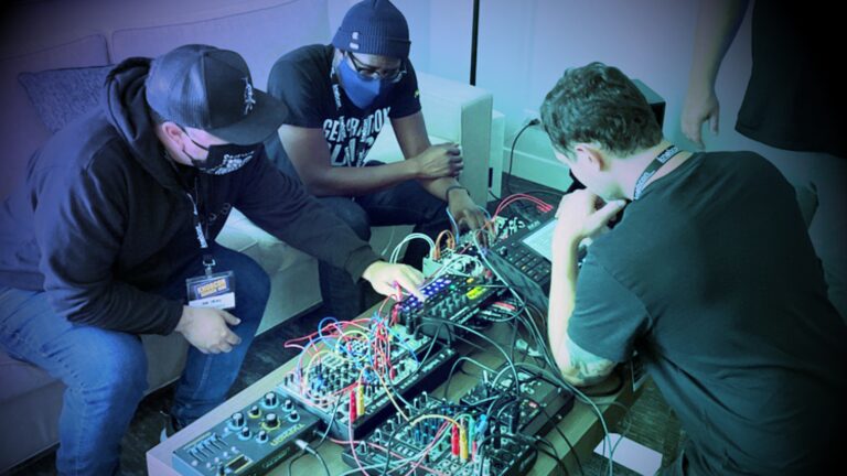 Three people crowded around a modular synth working on patching
