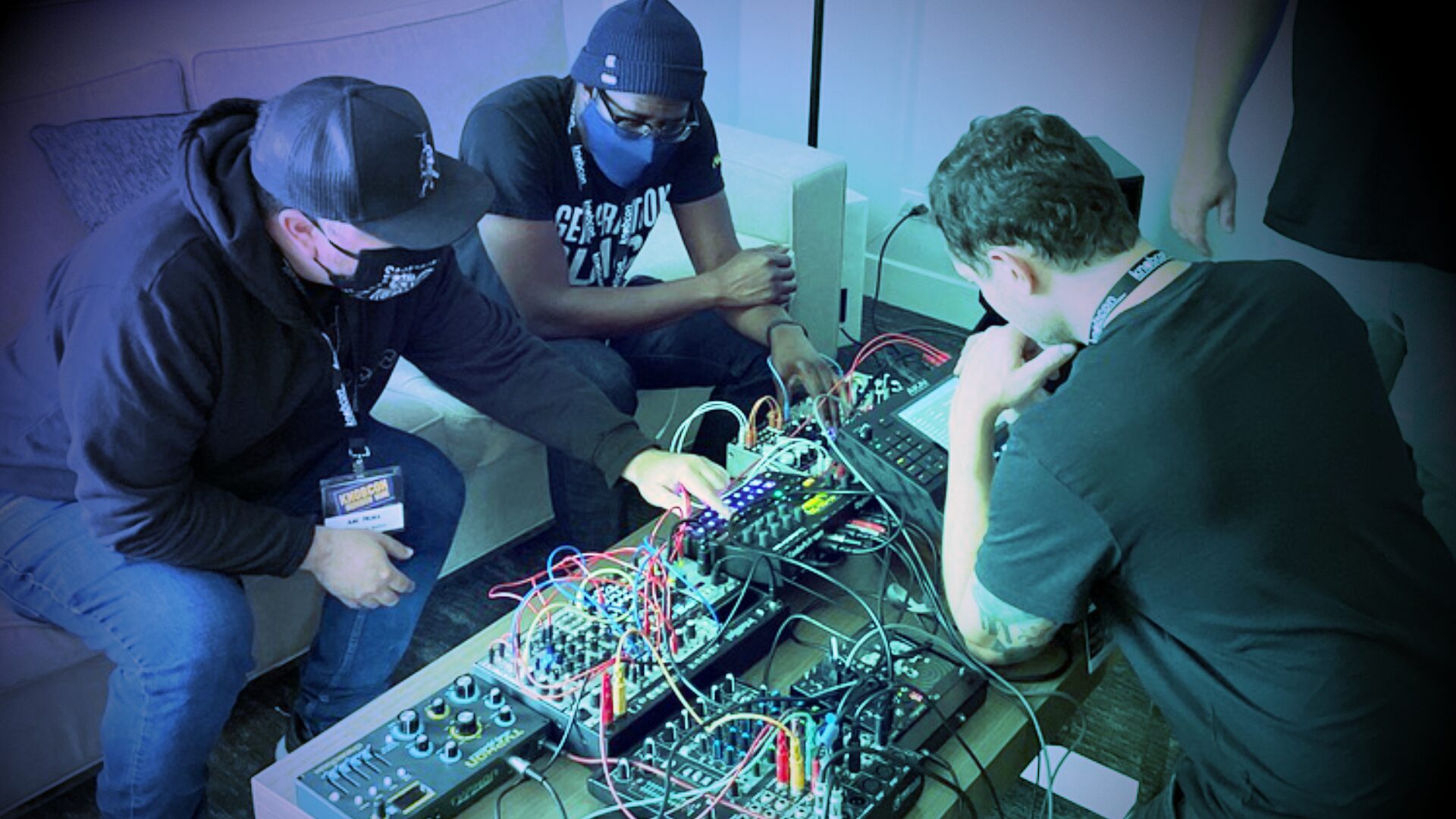 Three people crowded around a modular synth working on patching