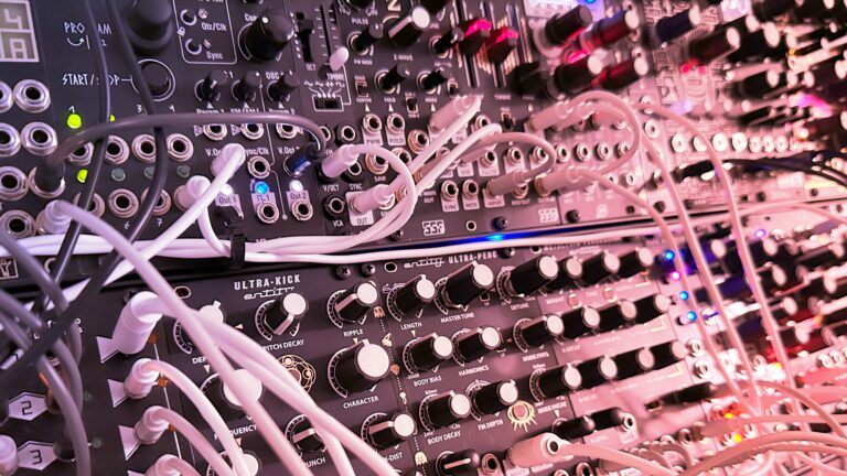 Dense Eurorack live rig with many white patch cables in pink lighting