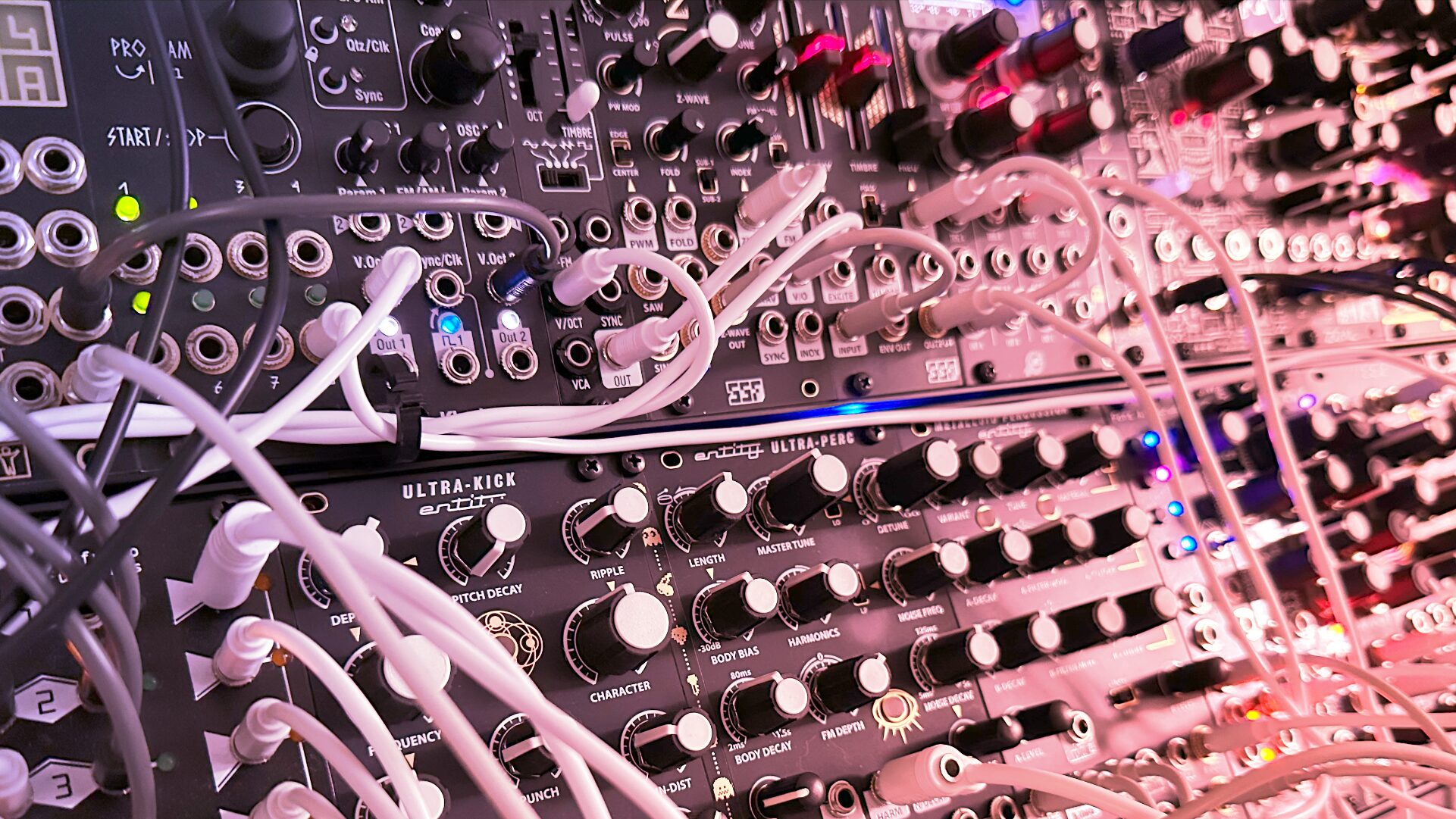 Dense Eurorack live rig with many white patch cables in pink lighting