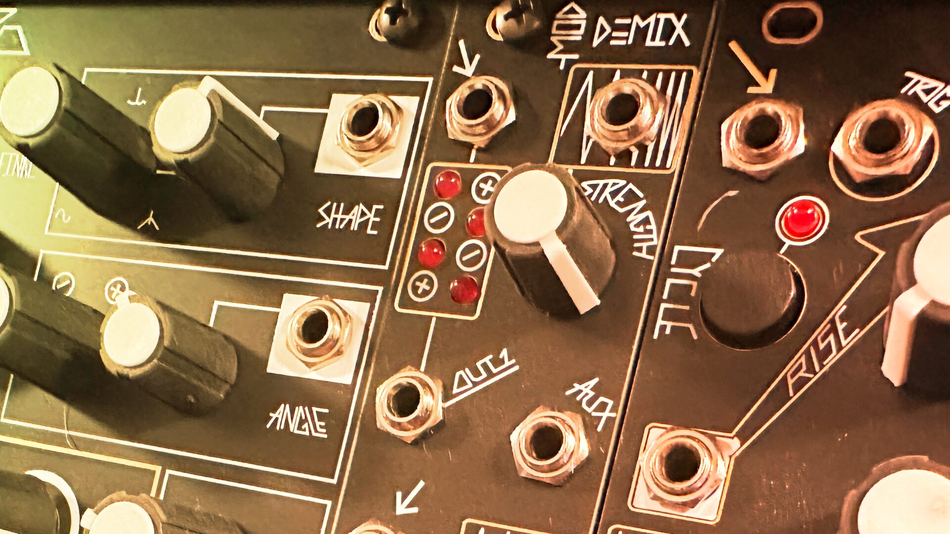 Close-up of Eurorack knobs and jacks in warm light with arrows printed on the panel