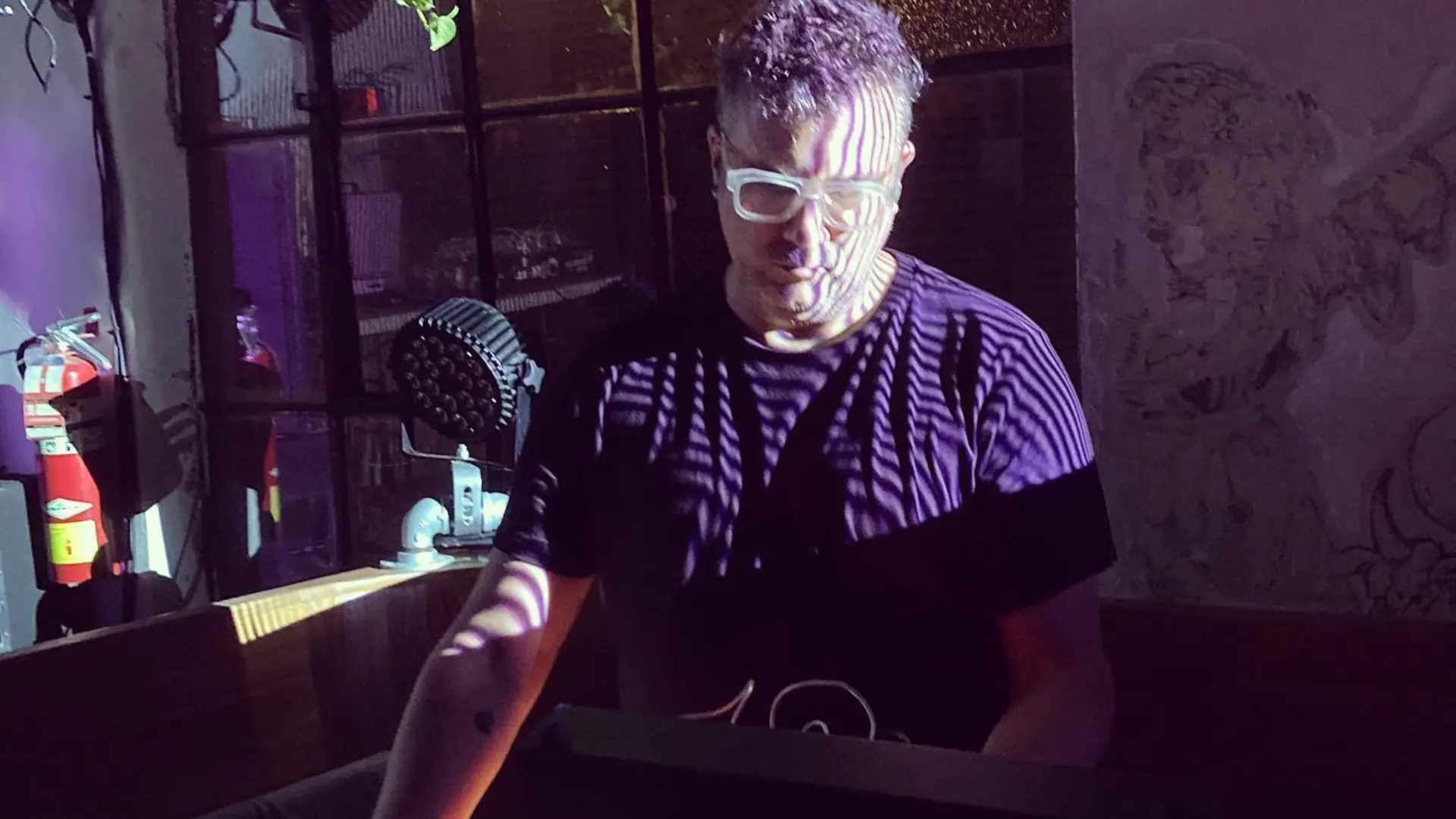 Performer wearing glasses at a modular synth during a live show under purple light